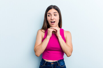 Young caucasian woman isolated on blue background praying for luck, amazed and opening mouth looking to front.