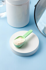 Collagen powder on spoon, podium and blue background. Natural beauty supplement for skin, bones. .