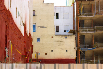 Dense, chaotic residential buildings in the old quarter of the city behind a fence. Construction or reconstruction of a house. Red, yellow and white building facades background. Urbanization concept.