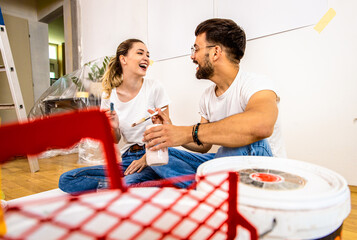 Young couple sitting on the floor choosing color for painting the wall in their home.
