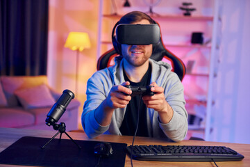 Fototapeta na wymiar With joystick. Portrait of gamer in VR glasses that playing game and streaming it online