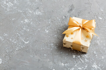 wrapped Christmas or other holiday handmade present in white paper with gold ribbon on colored background. Present box, decoration of gift on colored table, top view with copy space