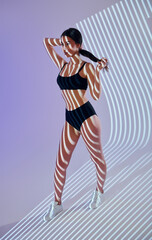 Fototapeta na wymiar Standing and posing. Beautiful young woman is in projector neon lights in the studio