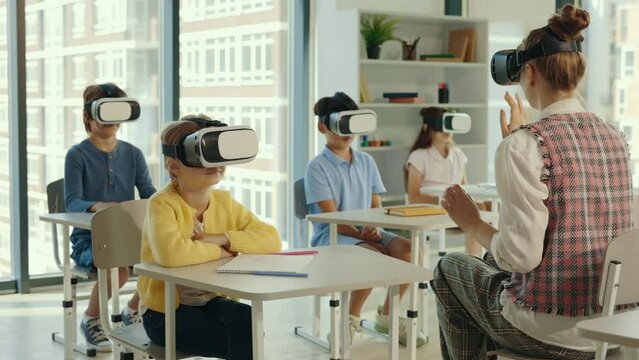 Multicultural school children using virtual reality headsets in classroom with teacher. Teacher is showing how to use virtual reality in the class. People technology and education concept.