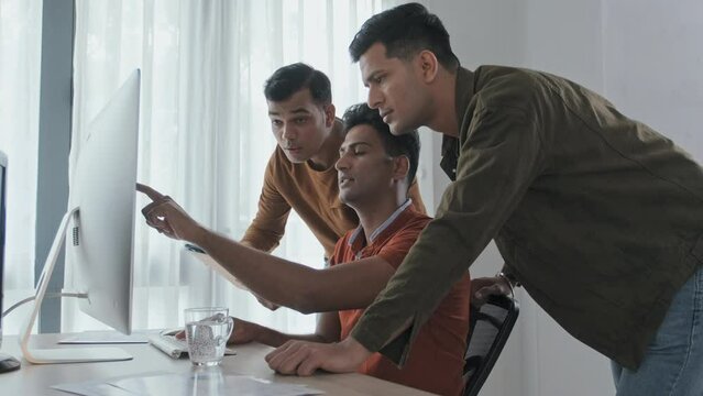 Medium slowmo of three male Indian programmers looking at computer monitor while discussing new software in office