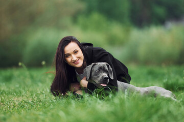 Laying down and smiling. Young brunette is having a walk with her dog outdoors