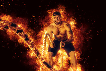 Fototapeta na wymiar Muscular man working out with battle ropes. Flame background