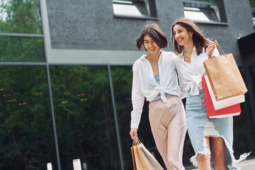 Smiling and talking. Two female friends have a shopping day. Walking outdoors with bags