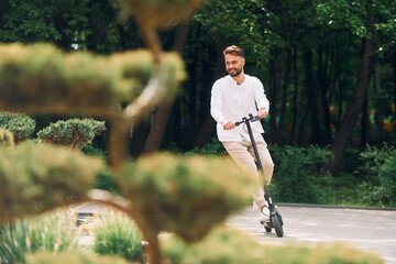 Beautiful trees and nature. Stylish man is with his scooter outdoors at daytime