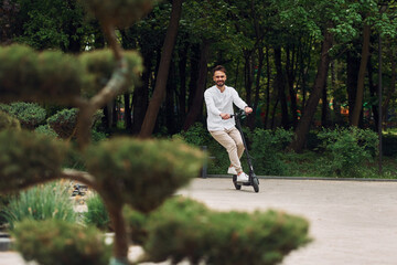 Beautiful trees and nature. Stylish man is with his scooter outdoors at daytime