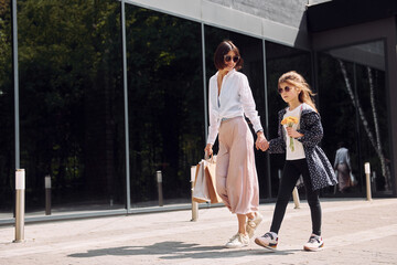 With bags in hand. Young mother with her daughter having a shopping day outdoors together