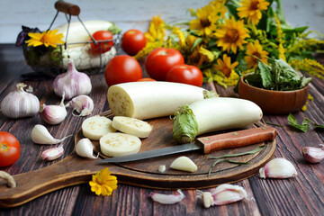 White eggplants on a wooden board, tomatoes, garlic, herbs, yellow flowers on a rustic table. Cooking vegetables, diet