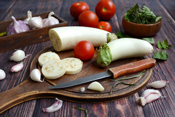 Close-up cutting board with white eggplant, tomatoes and garlic.Healthy food. Kitchen, autumn, harvest.