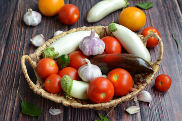View of a wicker basket with fresh tomatoes, eggplants, peppers, garlic on a rustic background.