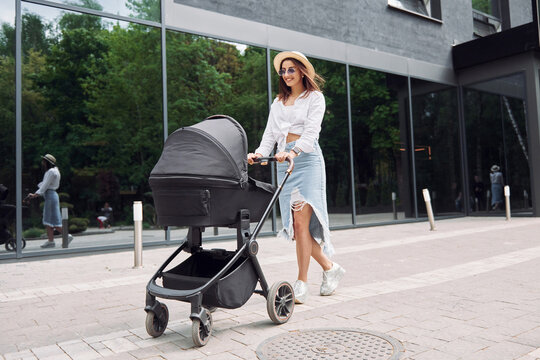 Young mother with baby carriage have a walk outdoors at daytime