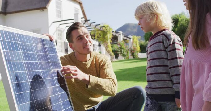 Video of happy caucasian father explaining solar panel to son and daughter in sunny garden