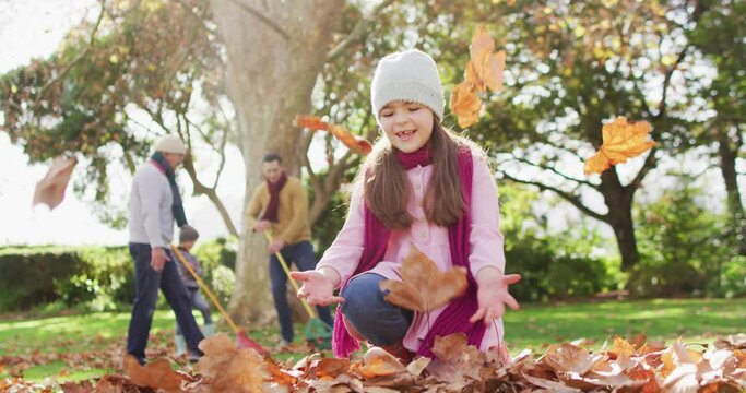 Video of happy caucasian daughter throwing autumn leaves in garden while family rakes them up behind