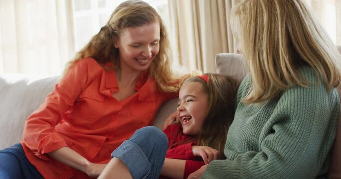 Video of happy caucasian daughter tickled by mother and grandmother sitting on couch