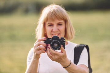 Using the camera. Making the photos. Senior woman having nice weekend outdoors on the field at sunny day