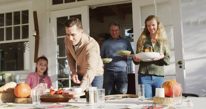 Video of happy caucasian parents, daughter and grandparents bringing food to table for family meal