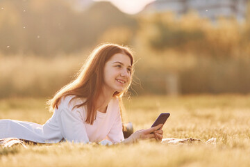 Using smartphone. Young girl is on the field at sunny daytime having nice weekend