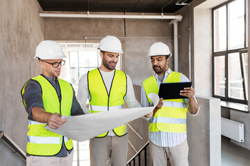 architecture, construction business and people concept - male architects in helmets with blueprint and tablet pc computer working in office building