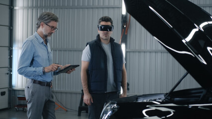 Manager in a suit and a mechanic in a virtual reality headset talking and standing near the car...