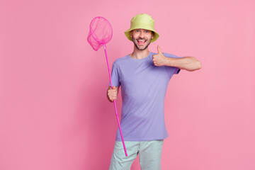 Photo of satisfied joyful guy hold net raise arm show super symbol have fun summer relax rest isolated on pink color background
