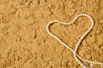 Heart made of white pearls on wet sand. Top view copy space.