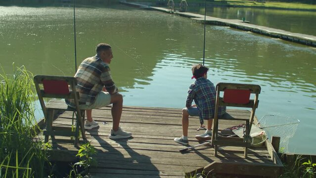 Joyful Cute Preadolescent Middle Eastern Son And Handsome Black Father Catching Fish On Fishing Rod, Expressing Excitement And Happiness While Multiethnic Family Enjoying Fishing On Lake At Sunrise.