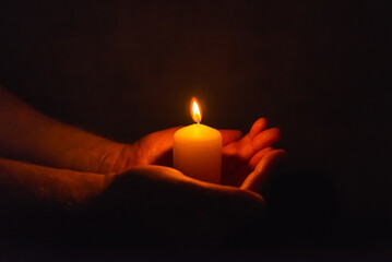 Burning candle in a mans hand religion concept.Candle in hands on a dark background.