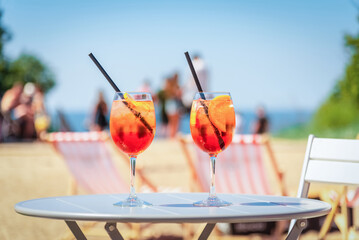 Two glasses of orange spritz aperol drink cocktail on table outdoors with sea and trees view...