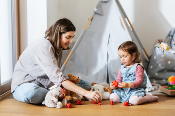 family, leisure and people concept - happy mother and little baby daughter playing tea party with...