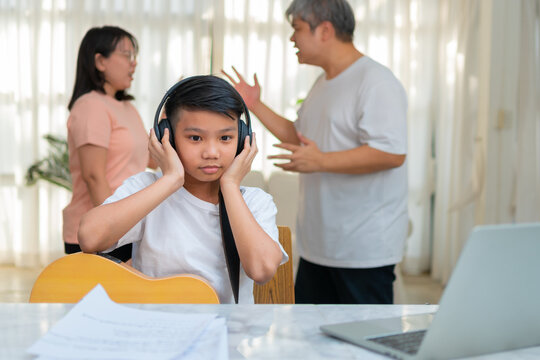 Asian boy kid wearing headphones and play loud music. so as not to hear quarrel while parents having fight or quarrel conflict at home. Unhappy problem in family, Domestic problems in the family.