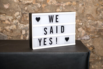 Lightbox /lightboard with text: We said yes! on black underground and stone wall in background. Used at weddings