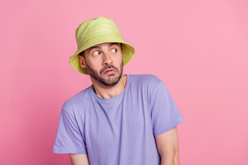 Photo of scared young man looks carefully empty space wear trendy violet clothes yellow cap isolated on pink color background