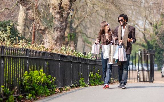 London Shoppers; Togetherness. A Young Mixed Race Couple Walking Home With Their Bags After A Day Out Shopping. From A Series Of Images.