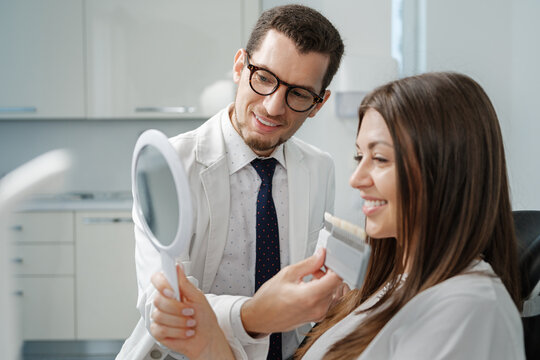 Young Man Dentist In White Coat Show Veneers Enamel Color Palette For Beautiful Patient Woman