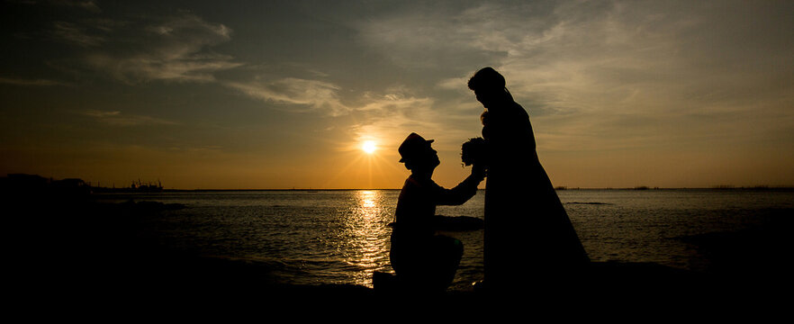 A silhouette of a young man, down on one knee and holding a bouquet, proposing to his girlfriend. will you marry me images.