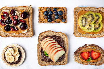 Various kind of open sandwiches with berries and fruits. Made from bread, such as wholegrain, rice crakers, crispbreads and different nut butter, such as peanut, crunchy cashew and almond butter
