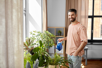 people, nature and plants care concept - happy smiling man watering flowers at home