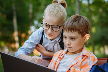 cute caucasian boys sitting on bench in park with laptop computer. Black screen