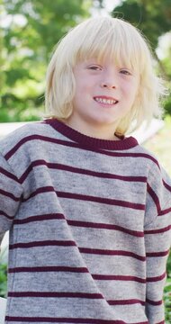 Vertical video portrait of happy caucasian boy with long blonde hair smiling in garden