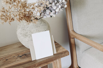 Boho fall still life photo. Rustic vase with dry hydrangea flowers in ceramic vase. Blank horizontal greeting card mockup on old wooden bench. Blurred linen sofa background. Scandinavian interior.
