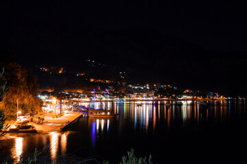 Night view of the embankment and promenade in the light of street lights and lighting of restaurants. small town surrounded by mountains in evening. Light reflections on sea water surface. cityscape