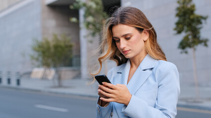 Close up portrait in city blonde serious girl business woman user stands on street looking at mobile phone wireless device gadget using smartphone app for chatting in network online reading news