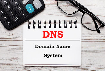 On a light wooden table calculator, glasses and a blank notepad with the text DNS Domain Name...