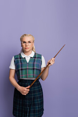 Blonde student in uniform and eyeglasses holding pointer isolated on purple