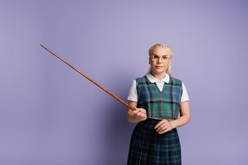 Blonde student in eyeglasses holding pointer on purple background