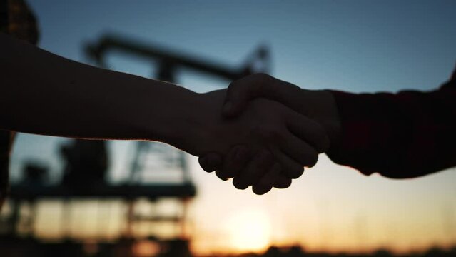 handshake oil contract. handshake a worker and businessman shaking hands against the backdrop of an oil pump. oil extraction business concept. silhouette close-up handshake business contract